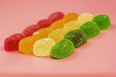 Renkli marmelat şekerlemeleri pembe arka planda sıra sıra serilmiş. Yüksek kalite fotoğraf