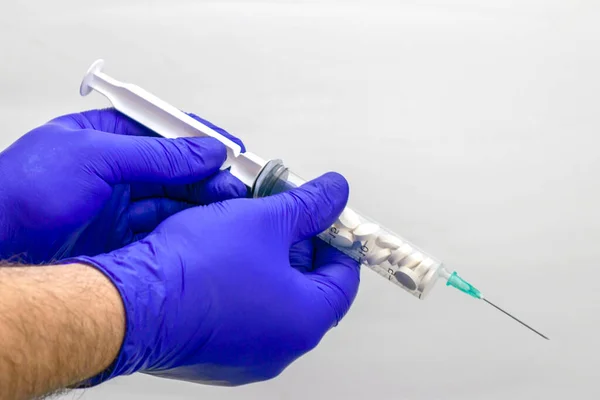 Concept vaccinatie geneeskunde apotheek een hand in een blauwe medische handschoen houdt een plastic spuit gevuld met pillen — Stockfoto