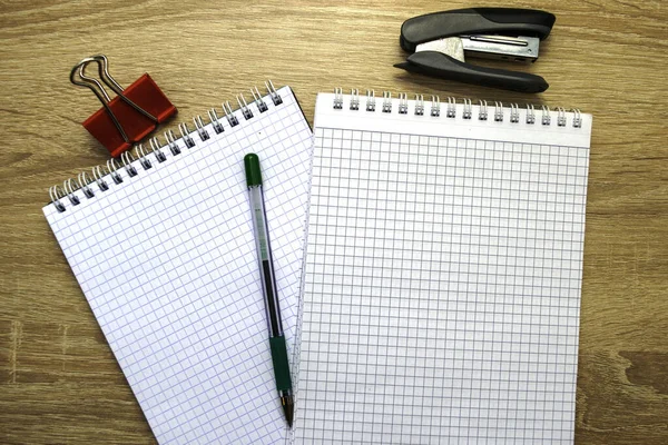 Twee open notitieblokken een vulpen een nietmachine en een paperclip op tafel — Stockfoto