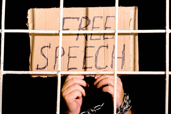 concept human rights freedom of speech hands shackled with an iron chain hold a cardboard sign with the inscription free speech behind an iron grate. High quality photo