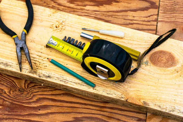 Measuring tape pliers pencil screwdrivers and a board on the carpenters workbench — Stock Photo, Image