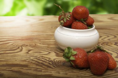 Tahta bir masada, yeşil yaprak kolajının arka planına karşı bir fincanda olgun sulu kırmızı çilekler. Yüksek kalite fotoğraf