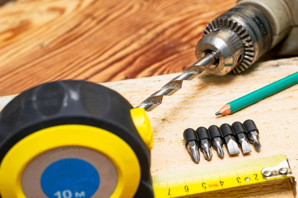 measuring tape measure drill with a drill pencil screwdrivers board on a wooden workbench. High quality photo