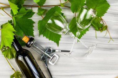 şarap şişesi tirbuşon, iki cam bardak ve üzüm dallarıyla boyanmış ahşap arka planda.