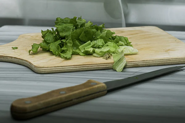 Lettuce leaves on a cutting board next to a knife on the table — Stock Photo, Image