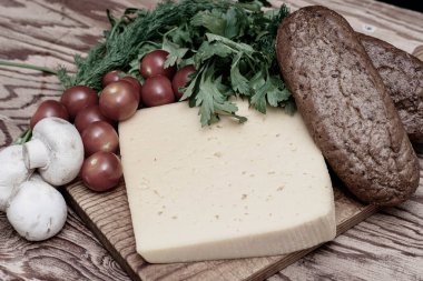 Bir parça peynir, kirazlı domates, mantar ve masanın üzerindeki tahta kesme tahtasının üzerinde çavdar ekmeği. Yüksek kalite fotoğraf