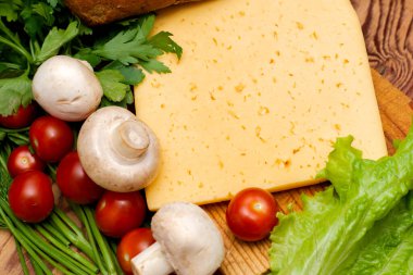 Bir parça peynir, marul, vişneli domates, mantar ve çavdar ekmeği masanın üzerinde ahşap kesim tahtasının üstünde.