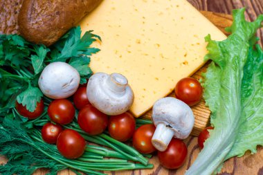 Bir parça peynir, marul, vişneli domates, mantar ve çavdar ekmeği masanın üzerinde ahşap kesim tahtasının üstünde.