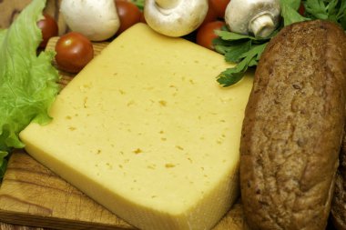 Bir parça peynir, marul, vişneli domates, mantar ve çavdar ekmeği masanın üzerinde ahşap kesim tahtasının üstünde.