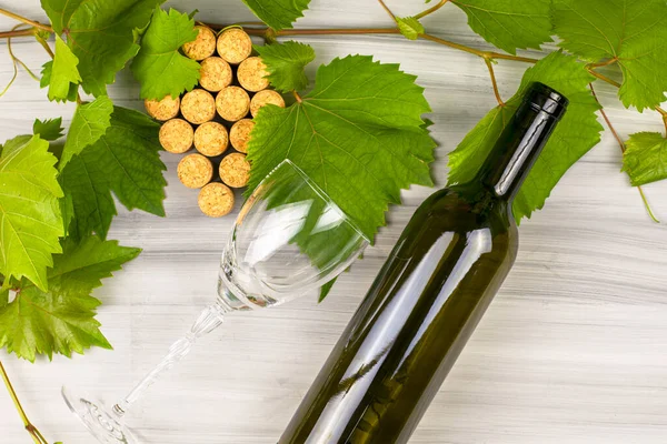 wine corks are laid out in the form of a grape brush grape branches a bottle of wine and a glass glass on a painted wooden background. High quality photo