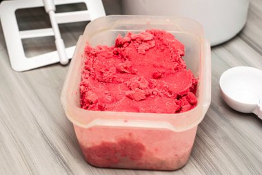 Masanın üzerinde, dondurma kaşığı ve dondurma makinesinin yanında duran plastik bir kapta ev yapımı vişneli dondurma. Yüksek kalite fotoğraf