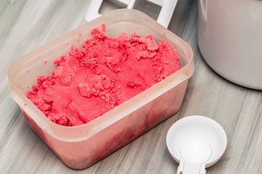 Masanın üzerinde, dondurma kaşığı ve dondurma makinesinin yanında duran plastik bir kapta ev yapımı vişneli dondurma. Yüksek kalite fotoğraf