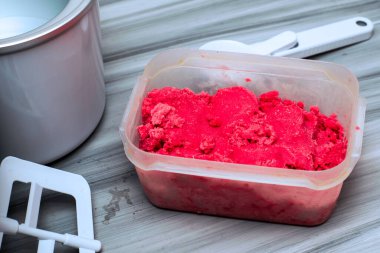 Masanın üzerinde, dondurma kaşığı ve dondurma makinesinin yanında duran plastik bir kapta ev yapımı vişneli dondurma. Yüksek kalite fotoğraf