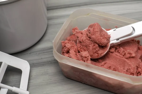 homemade cherry ice cream in a plastic container on the table with an ice cream spoon and an ice cream maker. High quality photo