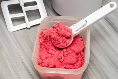 Masadaki plastik bir kapta, dondurma kaşığı ve dondurma makinesiyle ev yapımı vişneli dondurma. Yüksek kalite fotoğraf