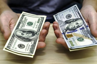 Bir adam yüz dolarlık banknotları masanın üzerindeki iki desteye koyar. Yüksek kalite fotoğraf