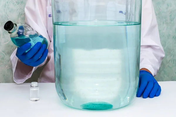 研究室の医療従事者は毒液のボトルを持っている彼の手にはテーブルの上に異なるサイズの他の容器がある 高品質の写真 — ストック写真