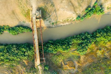 Bozkırdaki bir nehrin üzerinde eski bir demir köprü. Kırsal bir yolda. İnsansız hava aracından bir resim.