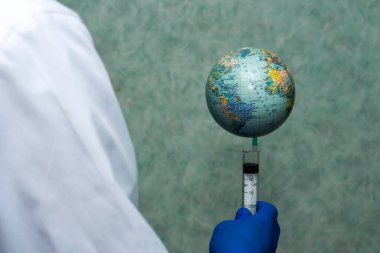 Beyaz önlüklü ve mavi koruyucu eldivenli bir doktor elinde bir şırınga tutuyor ve bu şırınganın üzerinde dünya konsepti aşısı var. Yüksek kalite fotoğraf