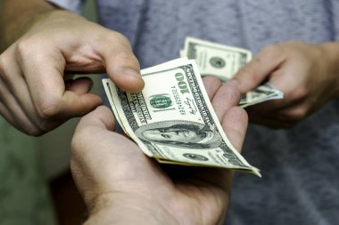 Bir kişi, bir diğerinin yanından yüz dolarlık banknotları sayarak geçer. Yüksek kalite fotoğraf