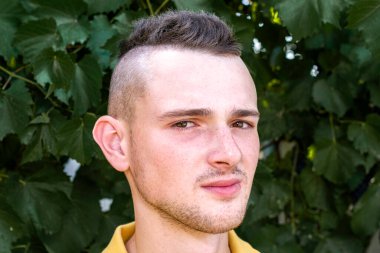 Yeşil yaprakların arka planında şık bir saç stili olan genç bir adam. Yüksek kalite fotoğraf