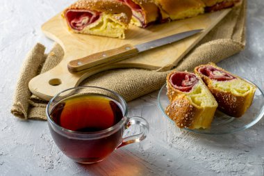 Kirazlı vanilyalı turta için bir bıçak ve açık gri bir yüzeyde bir fincan çay. İki parça turta bir tabağın üzerinde. Yüksek kalite fotoğraf