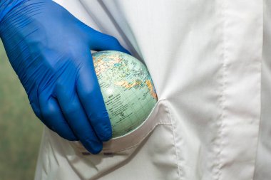 Beyaz önlüklü ve mavi eldivenli bir doktor bornozunun cebine dünya sağlık hizmetleri ilaçlarının bir küresini koydu. Yüksek kalite fotoğraf