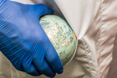Beyaz önlüklü ve mavi eldivenli bir doktor bornozunun cebine dünya sağlık hizmetleri ilaçlarının bir küresini koydu. Yüksek kalite fotoğraf