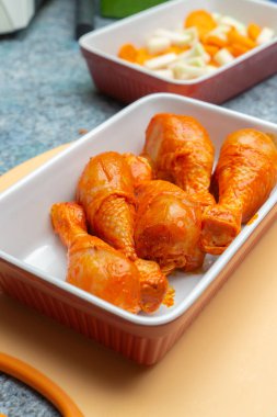 Taze terbiye edilmiş tavuk budu kasede ve arka planda bir kase sebze.