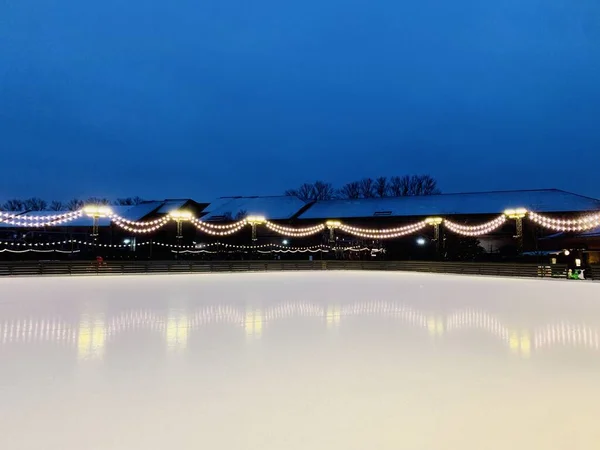 Φωτογραφία από το παγοδρόμιο τη νύχτα με φώτα. Πατινάζ παγοδρόμιο βρίσκεται στο πάρκο. Υπάρχει μια γιρλάντα πάνω από το παγοδρόμιο. — Φωτογραφία Αρχείου