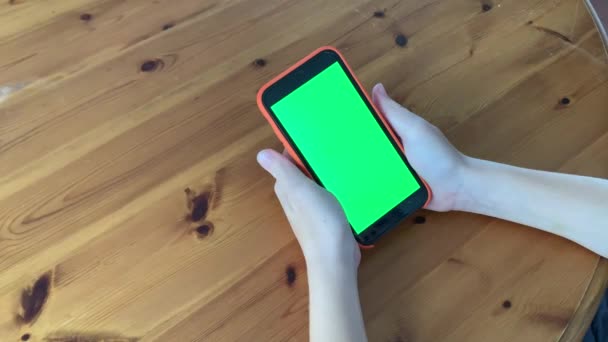มือเด็กวัยรุ่นใช้สมาร์ทโฟนหน้าจอสีเขียวนั่งอยู่บนโต๊ะ การสื่อสารทางธุรกิจออนไลน์ รูปแบบโครเมคกี้ แตะหน้าจอสัมผัสที่ว่างเปล่า เครือข่ายสังคม การสนทนาทางอินเทอร์เน็ต . — วีดีโอสต็อก