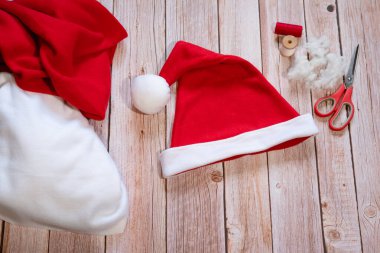 Noel Baba 'nın kırmızı şapkasını yaratma konusunda mastır. Hazır el yapımı Noel Baba şapkası açık ahşap bir masanın üzerinde, kumaş ve dikiş aksesuarlarının yanında. Adım adım talimatlar. Adım 20.