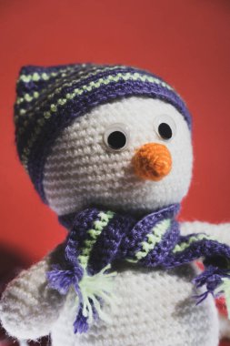 Şapkalı beyaz kardan adam. Parlak kırmızı arka planda el yapımı Noel oyuncağı. Havuçlu bir kardan adamın portresi..