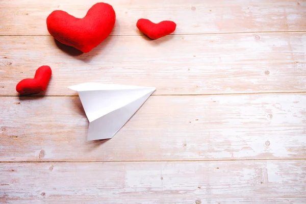 Instructions step by step. Do it yourself at home. Paper airplane the art of origami. DIY for Valentines day. White paper airplane on wooden table next to three red toy hearts. Step 7.