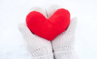 Bej eldivenli kumaştan yapılmış kırmızı yumuşak kalp oyuncağını yeni yağmış beyaz karın arka planında tut. Sevgililer Günü için yaratıcı tebrik kartı.