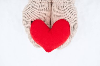 Bej eldivenli kumaştan yapılmış kırmızı yumuşak kalp oyuncağını yeni yağmış beyaz karın arka planında tut. Sevgililer Günü için yaratıcı tebrik kartı.