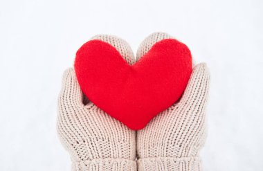 Bej eldivenli kumaştan yapılmış kırmızı yumuşak kalp oyuncağını yeni yağmış beyaz karın arka planında tut. Sevgililer Günü için yaratıcı tebrik kartı.