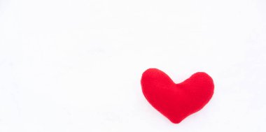 Küçük kırmızı oyuncak kalp beyaz karın üzerinde yatıyor. Sevgililer Günü tebrik kartı ve tebrik mesajın için bir sürü boş yer..