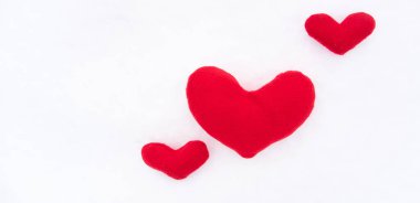 Beyaz karın üzerinde el yapımı kumaştan yapılmış üç adet kırmızı, yumuşak ve küçük oyuncak kalp var. Sevgililer Günü tebrik kartı ve tebrik mesajın için bir sürü boş yer..