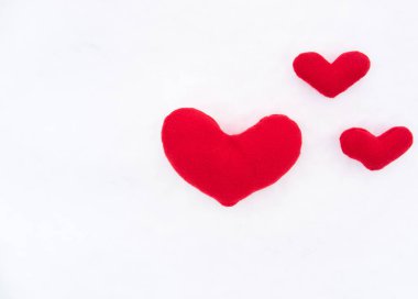 Beyaz karın üzerinde el yapımı kumaştan yapılmış üç adet kırmızı, yumuşak ve küçük oyuncak kalp var. Sevgililer Günü tebrik kartı ve tebrik mesajın için bir sürü boş yer..