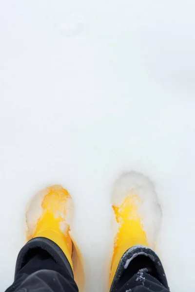 In yellow rubber boots, can walk in snow and measure depth of snowdrifts. View of feet in boots from above. Warm and comfortable shoes for any wet weather and cold.