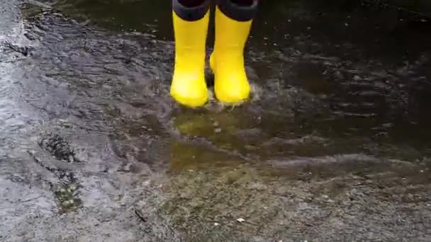 穿着黄色橡胶靴跳过水坑 在雨中散步 享受童年的坏天气 在潮湿的水坑中奔跑 没有脸的腿录像 — 图库视频影像