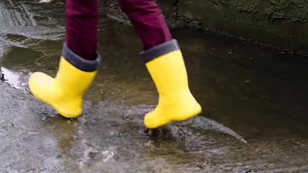 黄色のゴムブーツで水たまりを通って実行します 雨の中を歩くと 悪天候が子供の頃に落ち 湿った水たまりを通って実行してお楽しみください 顔のない足のビデオ — ストック動画
