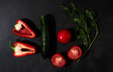 Kırmızı biber ve domates doğranmış, yeşil salatalık maydanozlu ve dereotlu siyah arka planda. Siyah mutfak masasında taze sebzeler. Minimalist restoran menüsü. Salata için malzemeler.