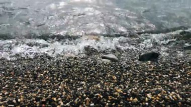 Dalgalar deniz kıyısında dönüyor. Şeffaf mavi sakin deniz. Sahilde kayalık sahil ve kum. Kıyıdan nefes kesici okyanus manzarası.