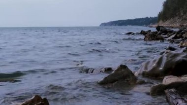 Yavaş çekim 4K videosu. Küçük deniz dalgaları kayalarda kırılır. Güzel deniz manzarası berrak mavi gökyüzü ve sakin deniz.