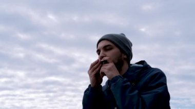 Gri şapkalı, beyaz sakallı çocuk mavi gökyüzüne yaslanıp ağzıyla müzik yaratıyor ve hayattan zevk alıyor. Genç erkek müzisyen mızıka çalıyor..