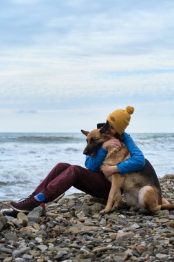 Çoban köpeğine iki elinle sıkıca sarıl. Genç, beyaz bir kadın boş zamanlarını köpekle sahilde oturarak geçiriyor. Kız ve Alman çoban köpeği temiz havada. Sahibi ve safkan köpeği sevmek.