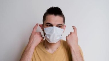 Genç, yakışıklı, beyaz, sakallı beyaz beyaz adam yüzünde beyaz koruyucu maskeyi çıkarıyor ve dikkatlice önüne bakıyor. Virüs ve bakterilere karşı bireysel koruma. Video görüntüleri 4k.
