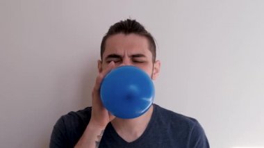 Mavi balonu ağızla şişir ve sonra uçup gitmesine izin ver. Sakallı, at kuyruklu, beyaz atlı, beyaz saçlı, genç, beyaz Avrupalı bir adam balonu arka planda şişiriyor..